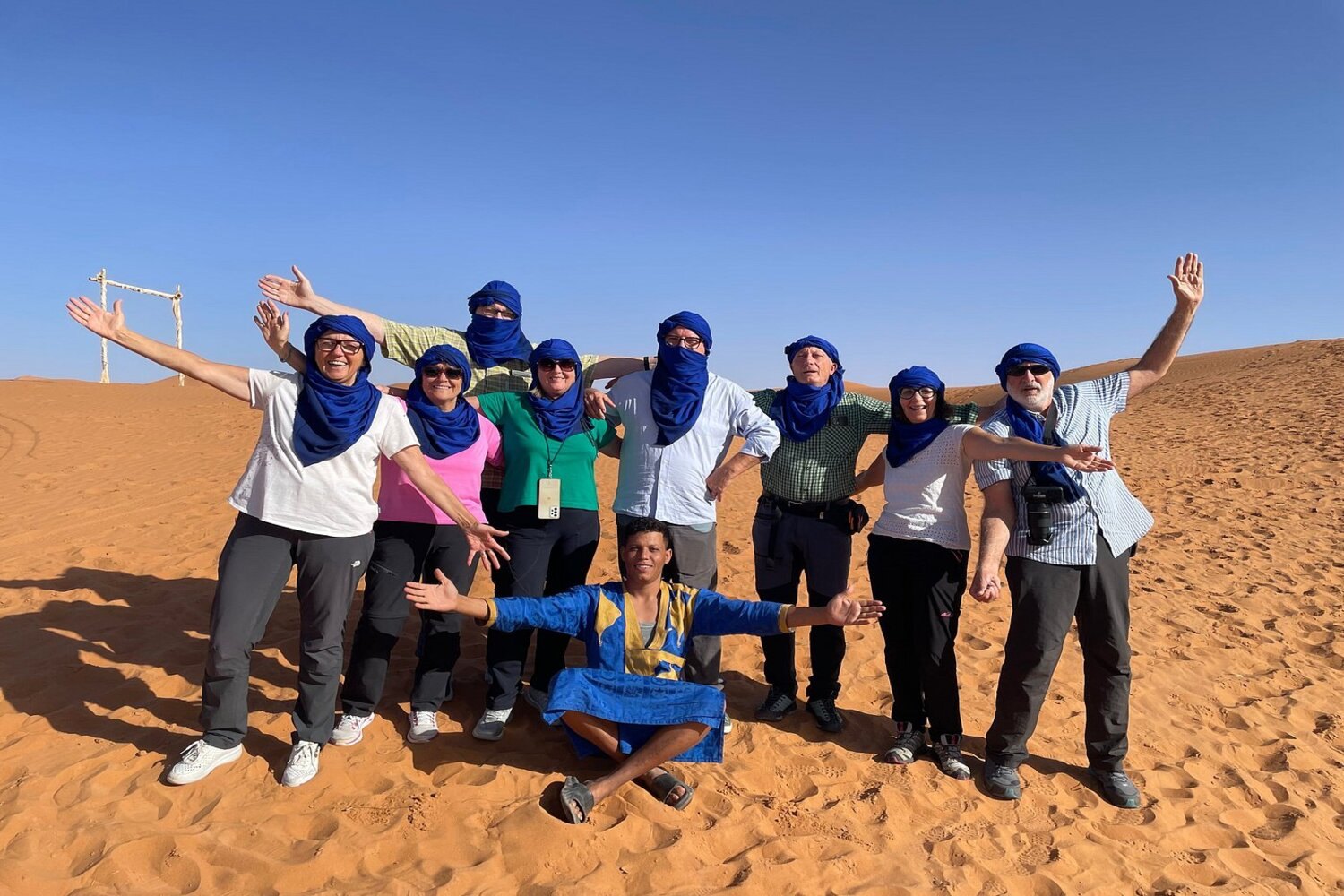 Group of travelers posing happily with their local desert host